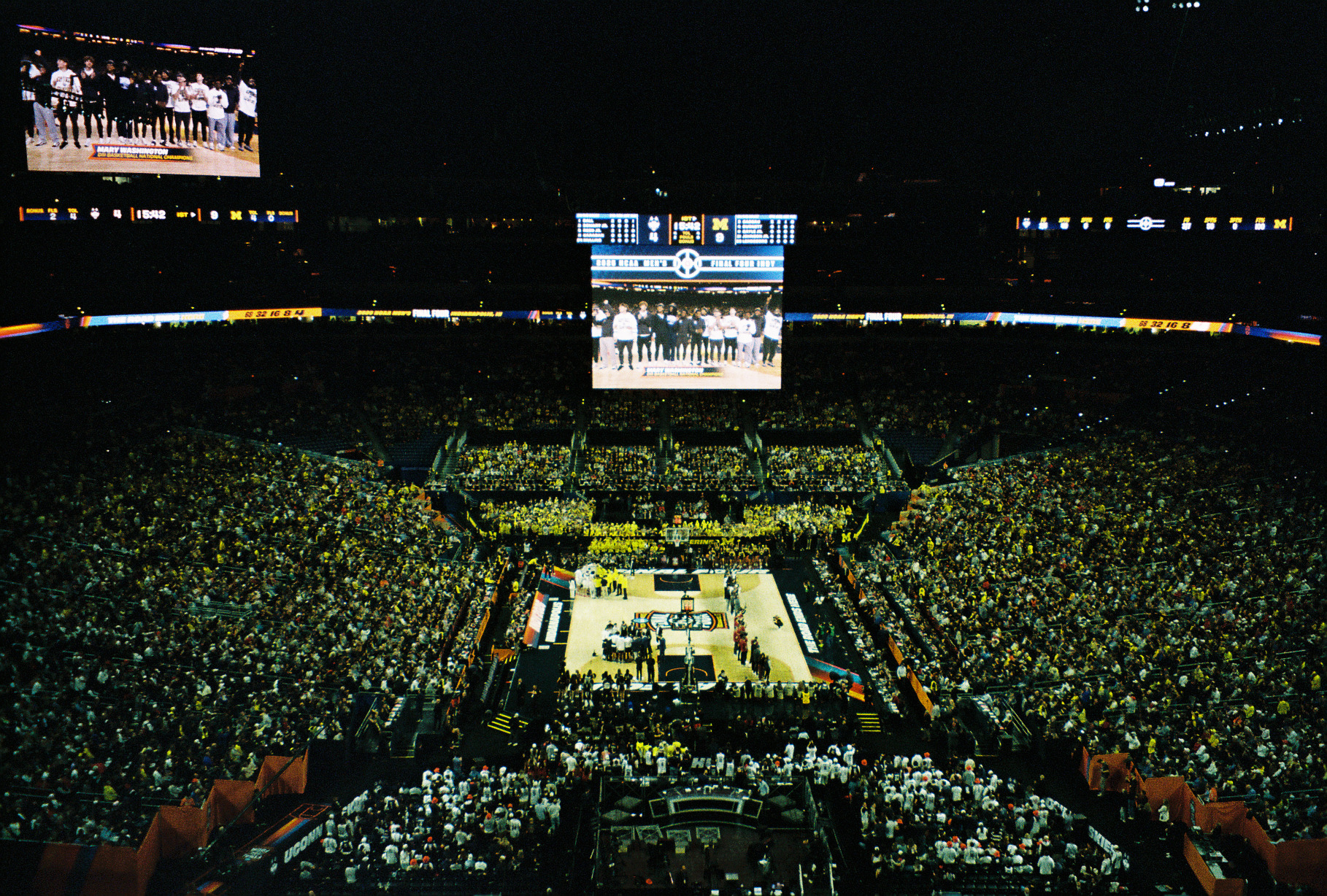 A packed arena during the NCAA Final Four, a jumbotron showing the Michigan team on the court below