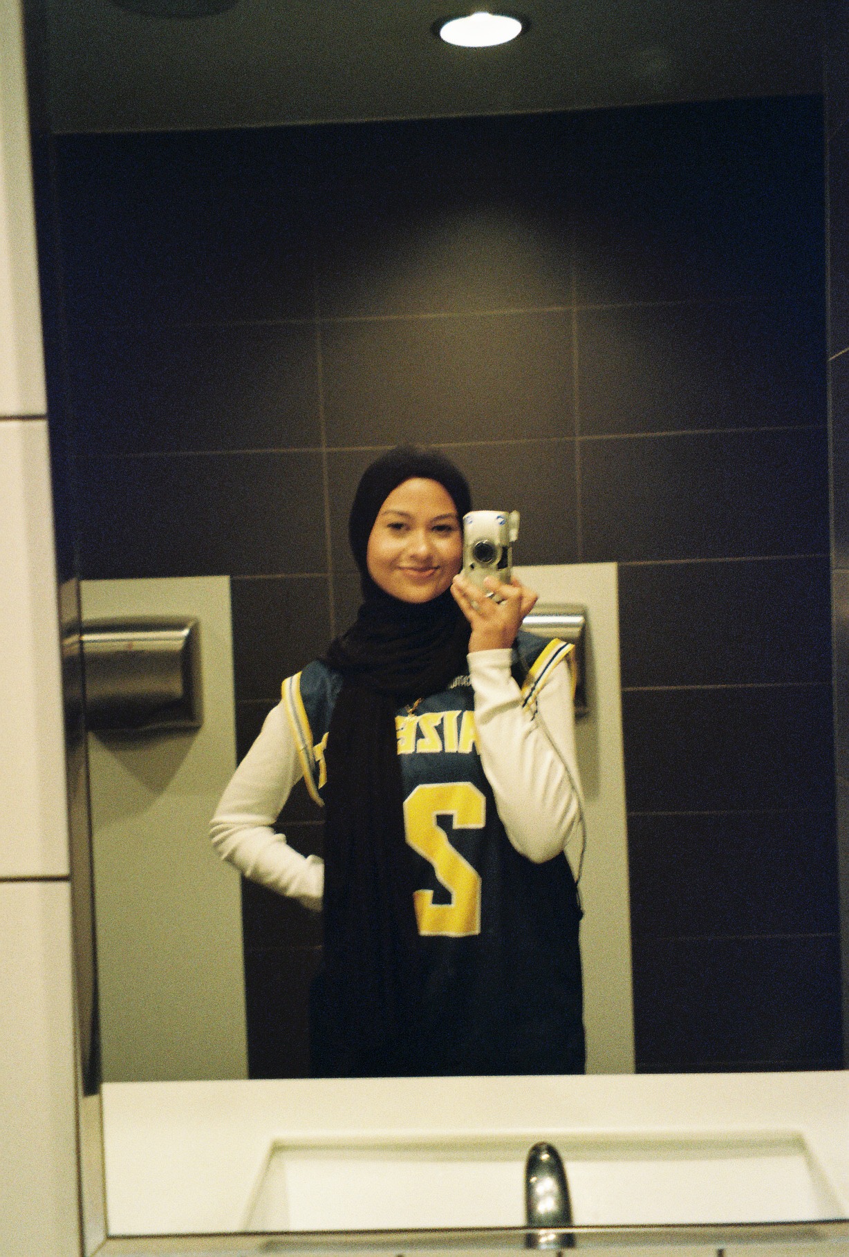 Tabassum taking a mirror selfie in a basketball jersey, holding a small digital camera