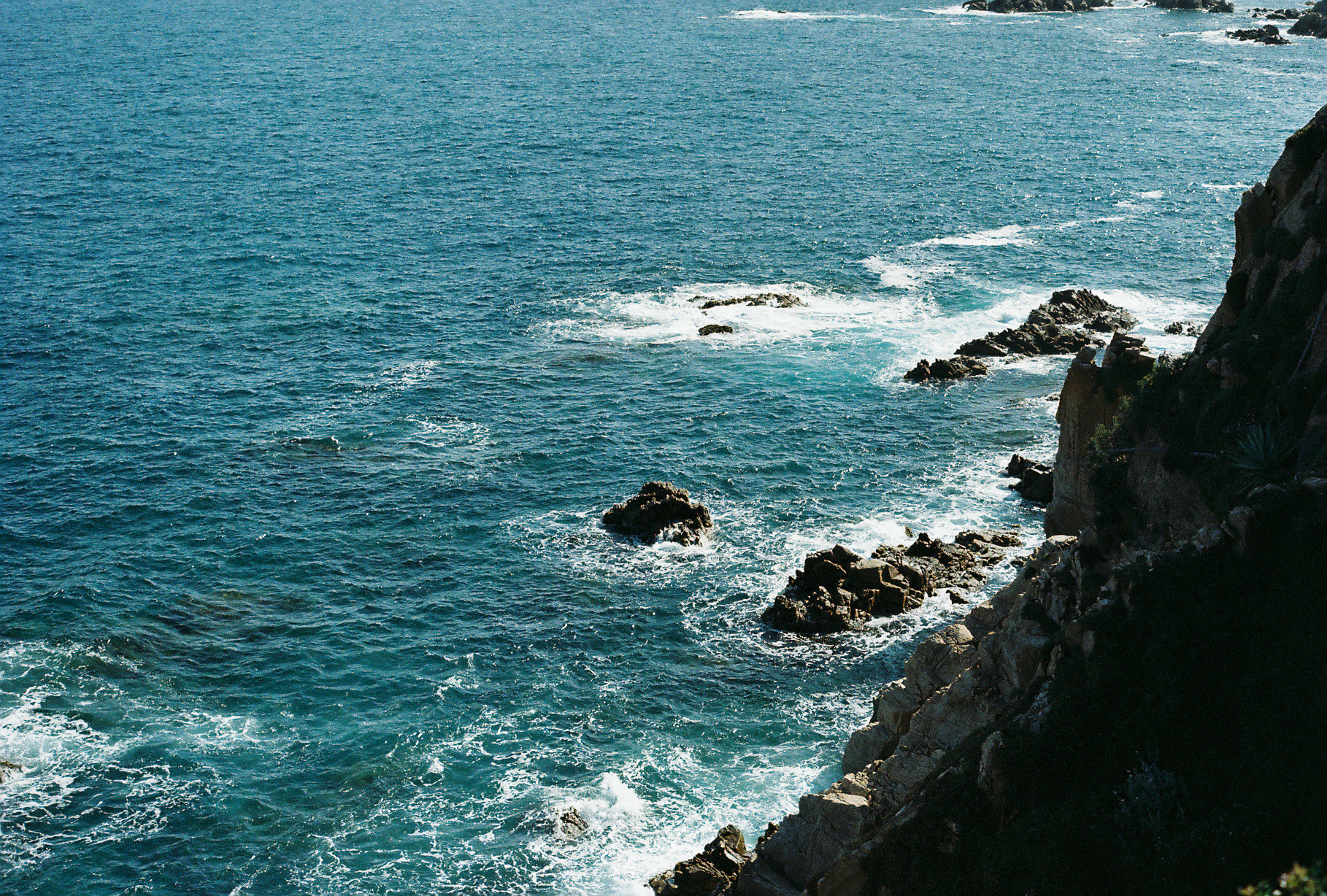 Turquoise water breaking against rocky cliffs along the Spanish coastline