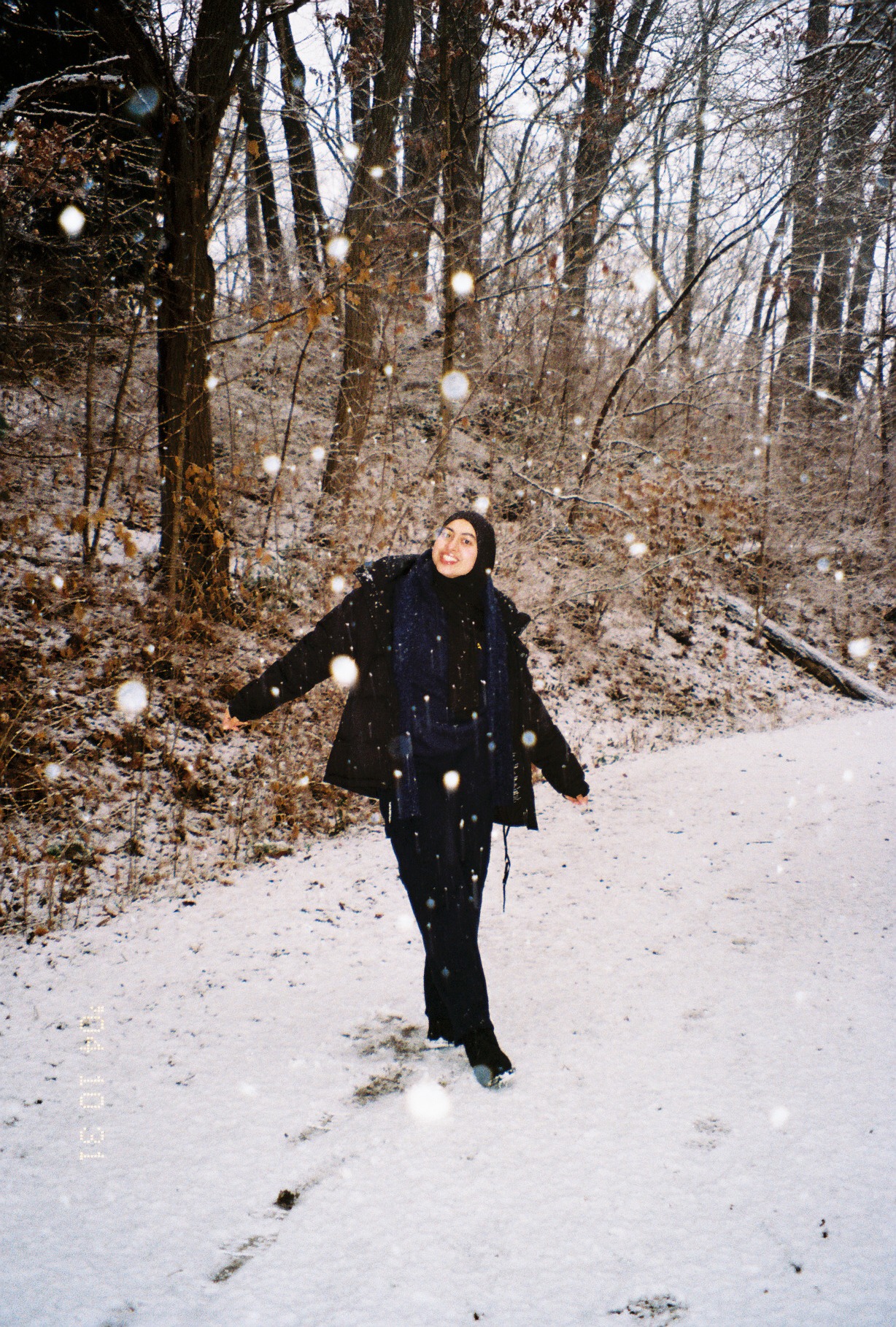 Tabassum's friend walking along a snowy Arb path with her arms out, smiling as snow falls around her