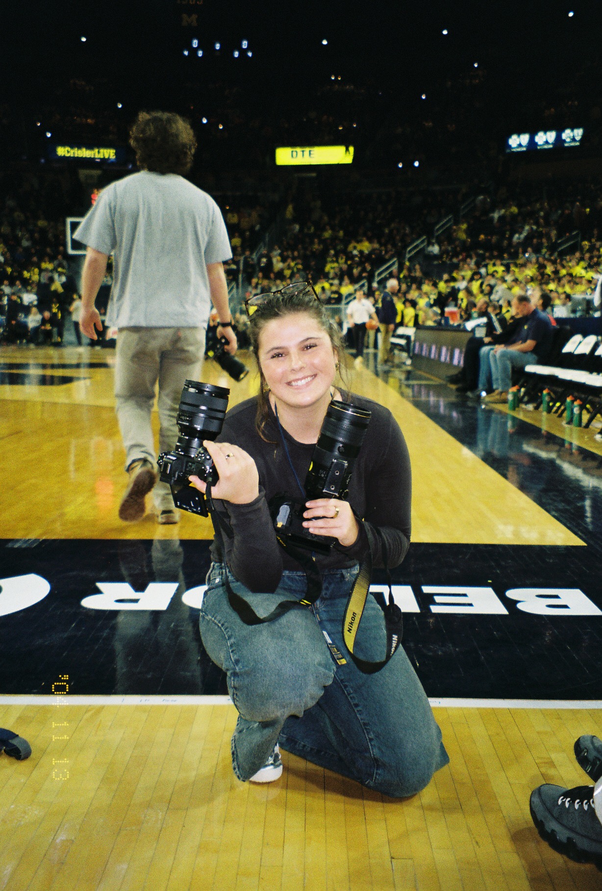 A female student photographer seated courtside holding a Nikon camera